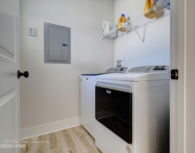 washroom with electric panel, washer and clothes dryer, and light hardwood / wood-style floors