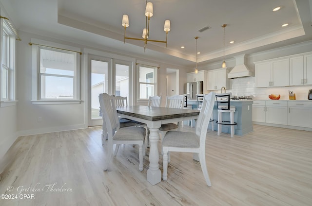 dining space with a healthy amount of sunlight, a raised ceiling, and light hardwood / wood-style floors