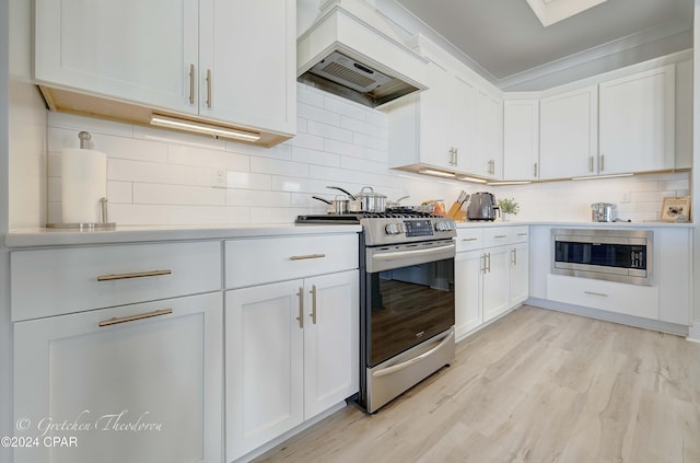 kitchen with backsplash, custom exhaust hood, stainless steel appliances, white cabinets, and light hardwood / wood-style floors