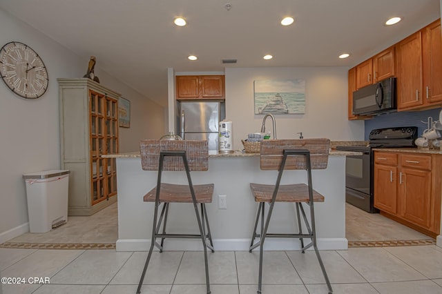 kitchen featuring a breakfast bar, light stone countertops, a center island with sink, and black appliances