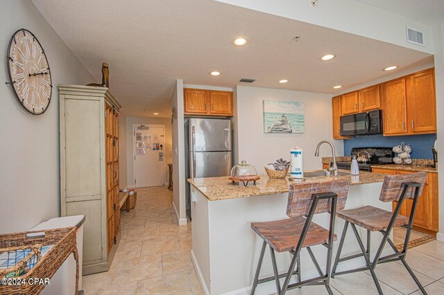 kitchen with a kitchen bar, a kitchen island with sink, light stone countertops, and black appliances