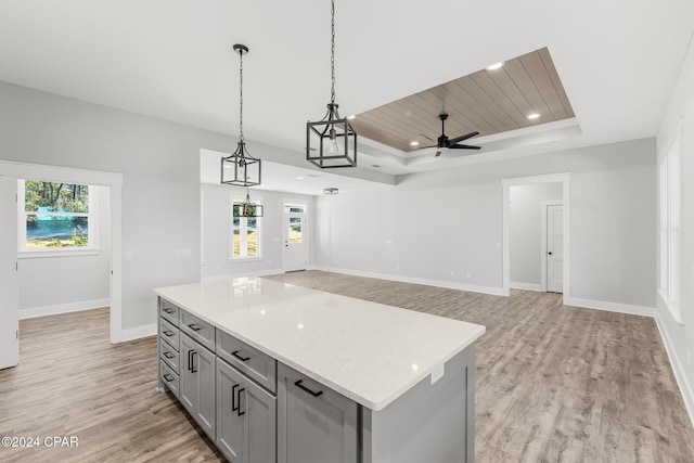 kitchen featuring ceiling fan, a center island, a raised ceiling, decorative light fixtures, and light wood-type flooring