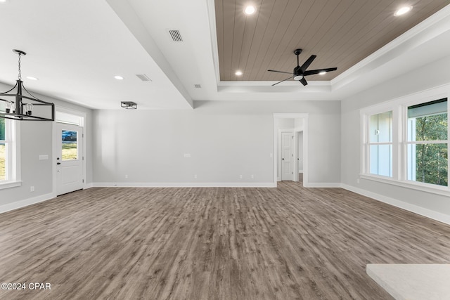 unfurnished living room with ceiling fan with notable chandelier, wood-type flooring, a wealth of natural light, and a tray ceiling