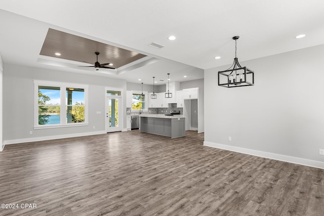 unfurnished living room with ceiling fan with notable chandelier, dark hardwood / wood-style floors, and a raised ceiling