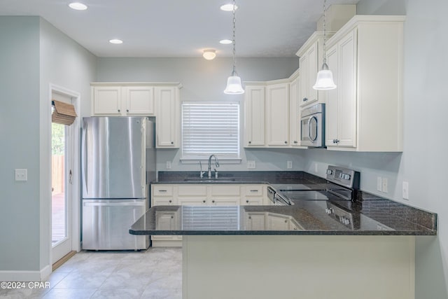 kitchen featuring kitchen peninsula, appliances with stainless steel finishes, dark stone counters, sink, and decorative light fixtures