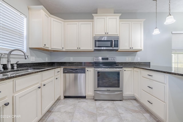 kitchen with sink, hanging light fixtures, dark stone countertops, a textured ceiling, and stainless steel appliances