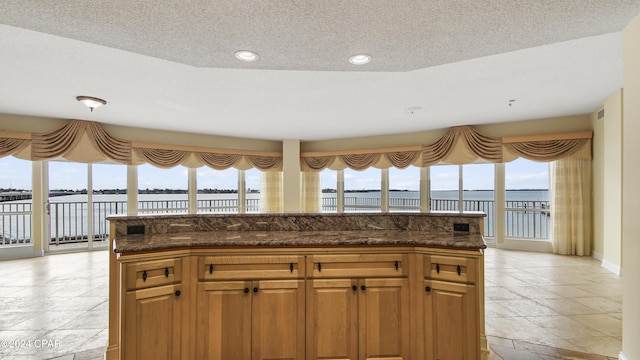 kitchen with a textured ceiling, a water view, and dark stone countertops