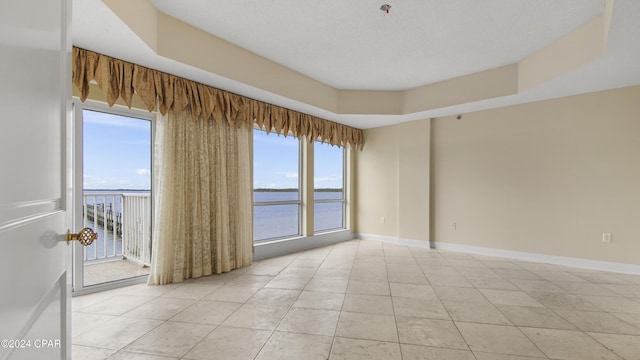 empty room featuring light tile patterned floors, a water view, a raised ceiling, and a healthy amount of sunlight