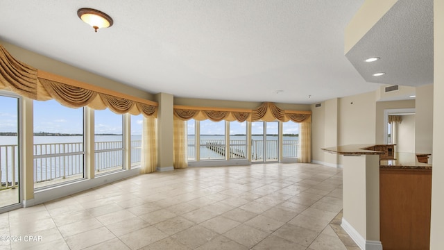 unfurnished living room with a wealth of natural light, light tile patterned floors, a water view, and a textured ceiling