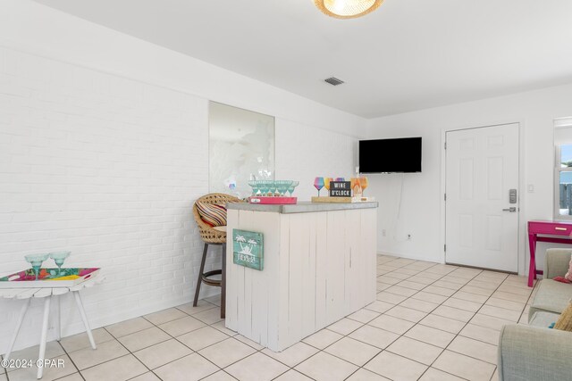 kitchen with brick wall, a breakfast bar area, and light tile patterned flooring