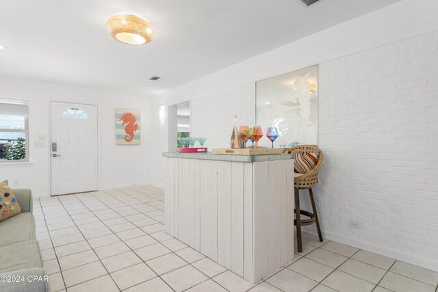 kitchen featuring brick wall, light tile patterned flooring, a healthy amount of sunlight, and a breakfast bar area