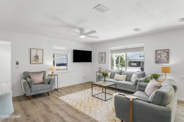 living room featuring ceiling fan, a textured ceiling, and light hardwood / wood-style floors