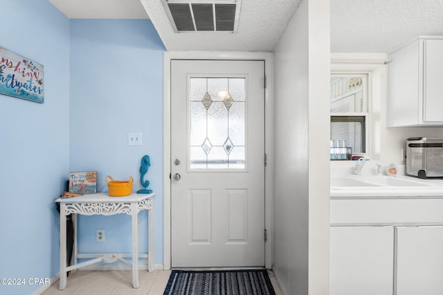 doorway to outside with a textured ceiling, light tile patterned floors, and sink