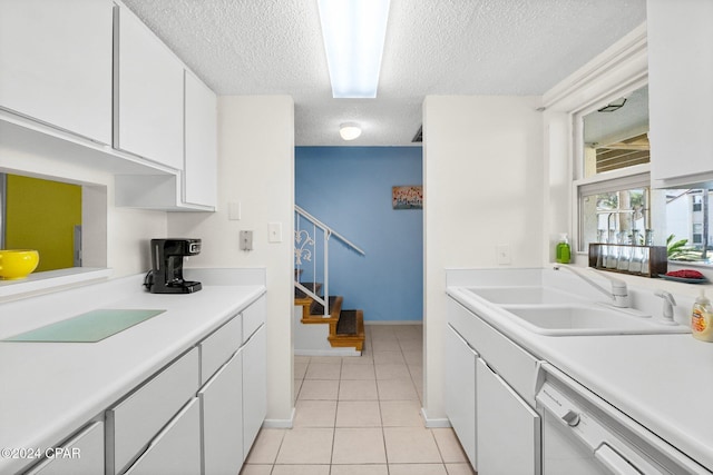 kitchen with white dishwasher, white cabinets, sink, light tile patterned floors, and a textured ceiling