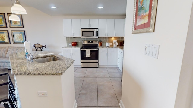 kitchen with pendant lighting, backsplash, sink, white cabinetry, and stainless steel appliances