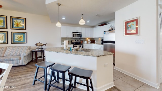 kitchen featuring light stone countertops, stainless steel appliances, decorative light fixtures, a kitchen island with sink, and white cabinets