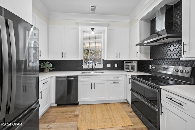 kitchen with white cabinetry, sink, wall chimney exhaust hood, light hardwood / wood-style floors, and appliances with stainless steel finishes