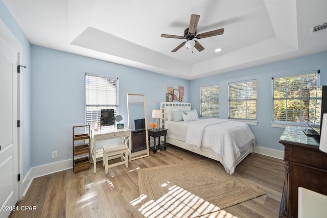 bedroom featuring hardwood / wood-style floors, ceiling fan, a tray ceiling, and multiple windows