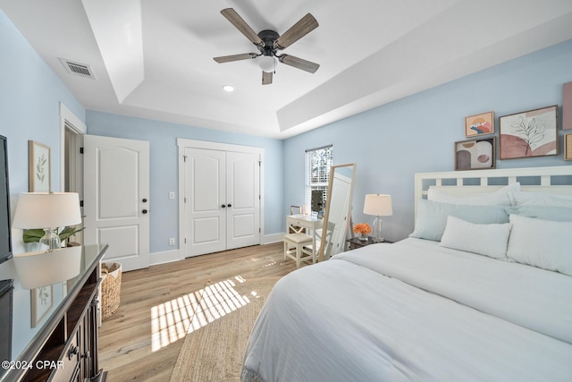 bedroom with a raised ceiling, a closet, light hardwood / wood-style flooring, and ceiling fan