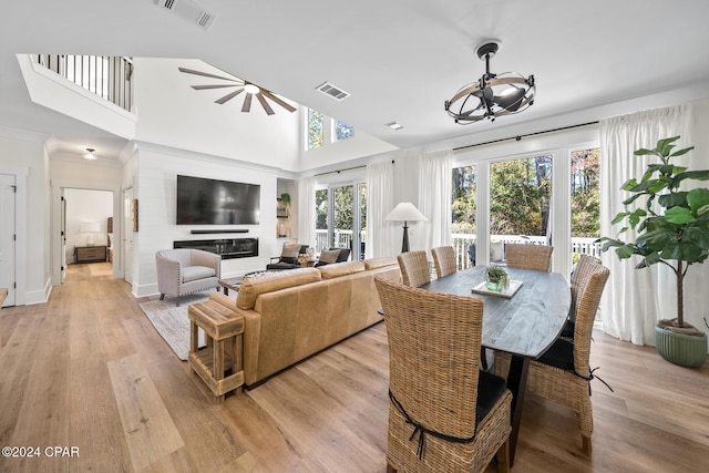 dining room featuring ceiling fan with notable chandelier, light hardwood / wood-style floors, and high vaulted ceiling