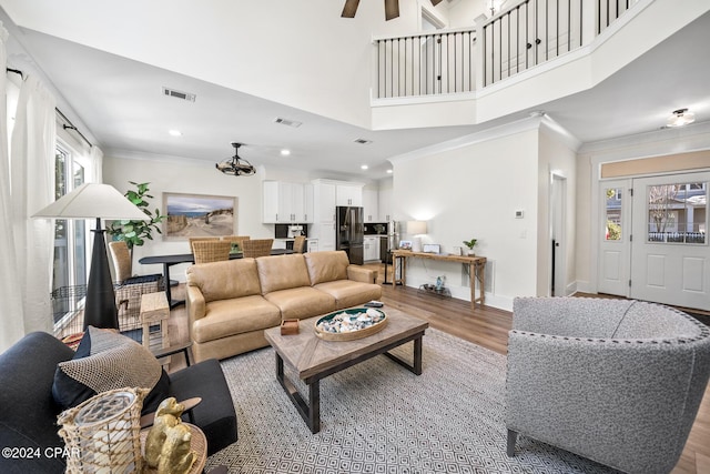 living room with a towering ceiling, wood-type flooring, ceiling fan with notable chandelier, and ornamental molding