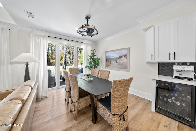 dining space featuring wine cooler, crown molding, light hardwood / wood-style floors, and a notable chandelier