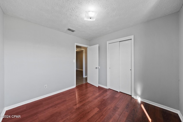 unfurnished bedroom with a textured ceiling, dark hardwood / wood-style flooring, and a closet