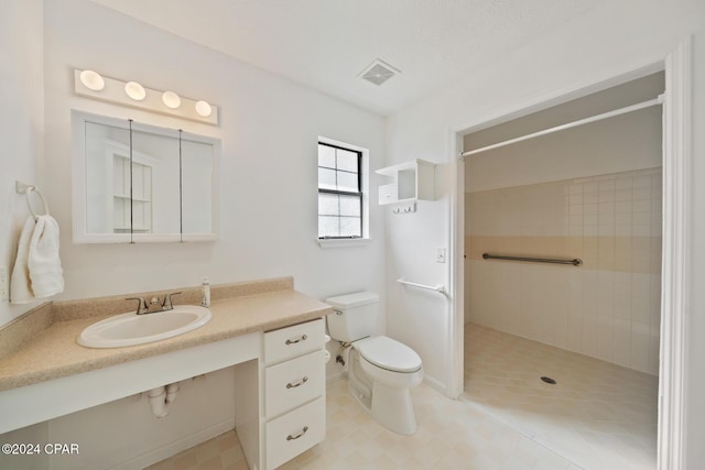 bathroom featuring toilet, a tile shower, and sink