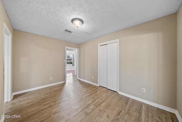 unfurnished bedroom with light wood-type flooring, a textured ceiling, and a closet