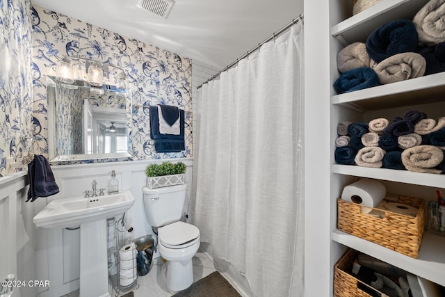 bathroom with toilet, wallpapered walls, visible vents, and wainscoting