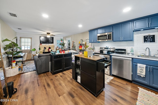 kitchen with stainless steel appliances, wood finished floors, a sink, visible vents, and blue cabinetry