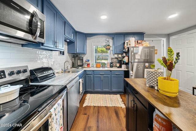 kitchen with stainless steel appliances, a sink, wooden counters, blue cabinetry, and backsplash