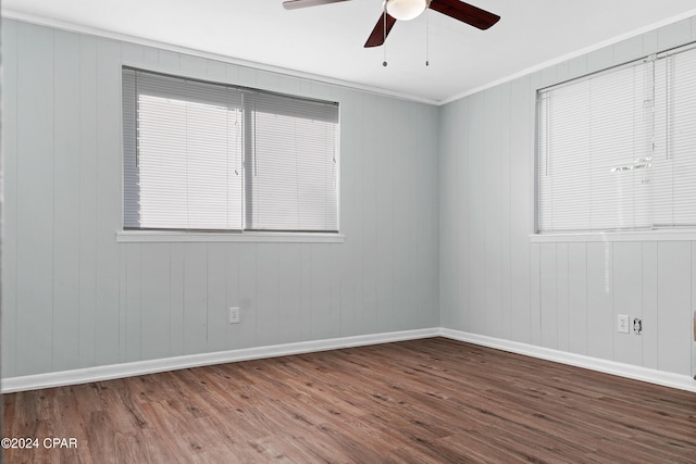 spare room featuring wood-type flooring, wooden walls, ceiling fan, and ornamental molding