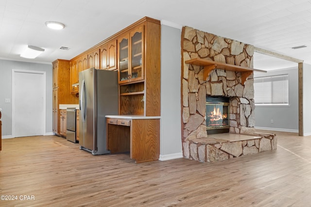 kitchen with a stone fireplace, stainless steel fridge with ice dispenser, crown molding, stove, and light hardwood / wood-style floors