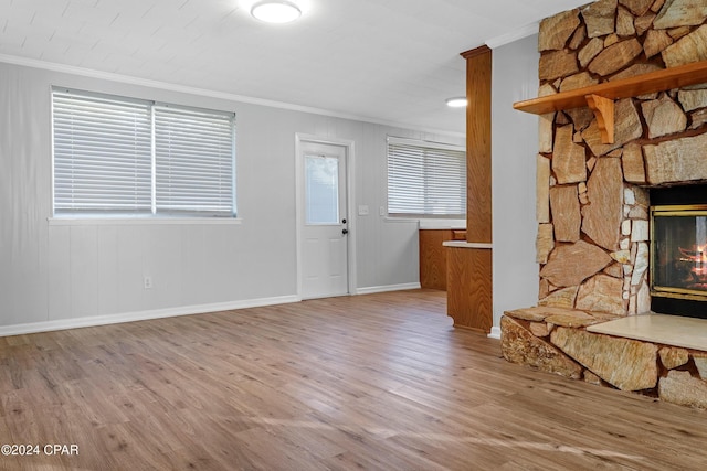 unfurnished living room with light wood-type flooring, a stone fireplace, plenty of natural light, and ornamental molding