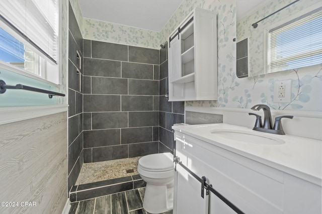 bathroom featuring tiled shower, vanity, toilet, and plenty of natural light