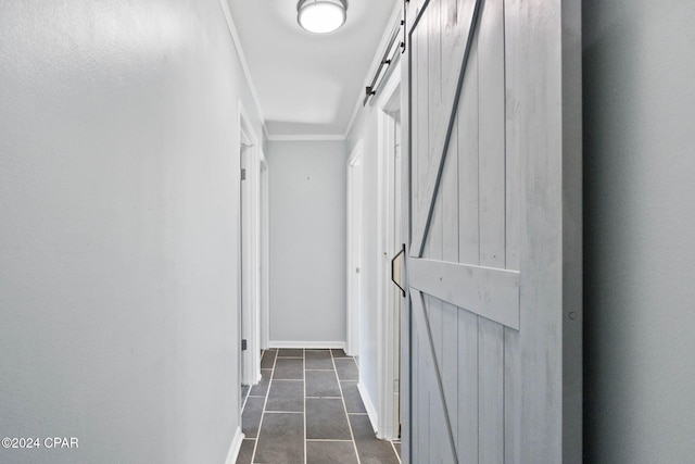 hall with a barn door, dark tile patterned flooring, and crown molding