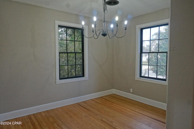 unfurnished dining area featuring a wealth of natural light, a chandelier, and wood-type flooring