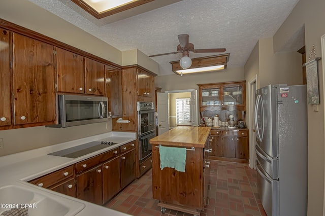 kitchen featuring wood counters, a textured ceiling, ceiling fan, black appliances, and a center island