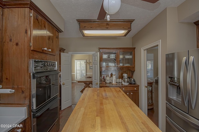 kitchen with wooden counters, a textured ceiling, black double oven, hardwood / wood-style floors, and stainless steel fridge with ice dispenser