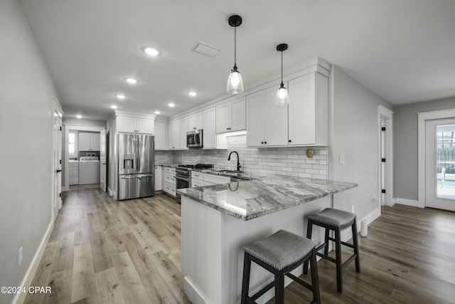 kitchen with white cabinets, kitchen peninsula, appliances with stainless steel finishes, and light hardwood / wood-style flooring