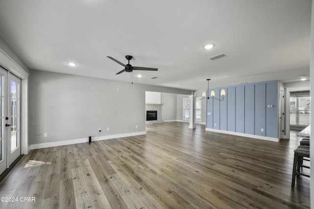 unfurnished living room featuring a wealth of natural light, hardwood / wood-style floors, and ceiling fan with notable chandelier