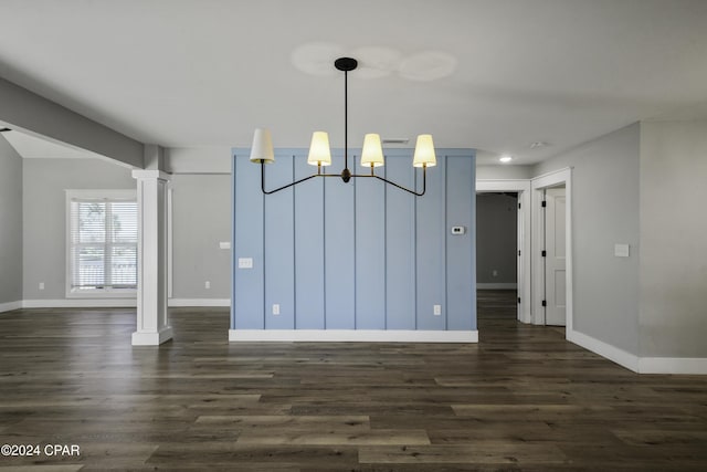 unfurnished dining area featuring decorative columns, dark hardwood / wood-style floors, and an inviting chandelier