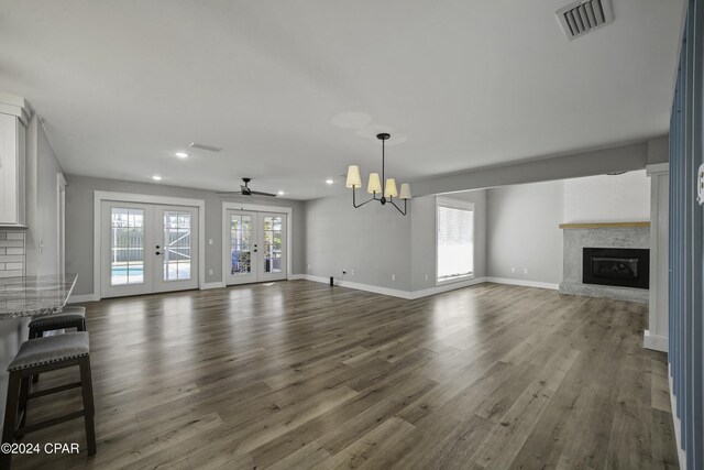 unfurnished living room with plenty of natural light, dark hardwood / wood-style flooring, ceiling fan with notable chandelier, and french doors