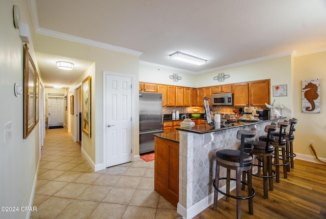 kitchen with stainless steel appliances, kitchen peninsula, crown molding, decorative backsplash, and a breakfast bar