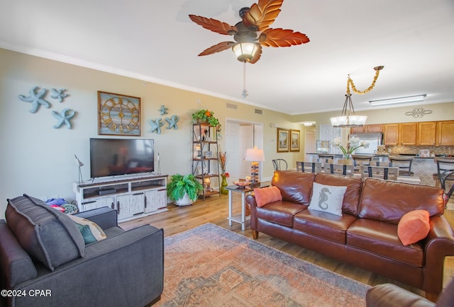 living room with ceiling fan with notable chandelier, light wood-type flooring, and ornamental molding