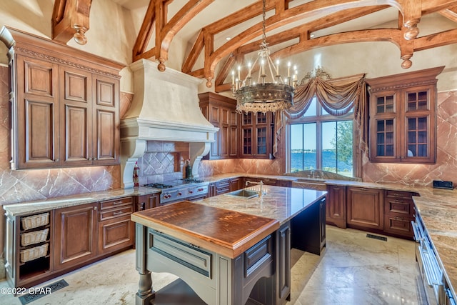 3730 Preserve Bay Blvd, Panama City, FL 32408 - kitchen featuring a kitchen island with sink, an inviting chandelier, decorative light fixtures, decorative backsplash, and custom range hood