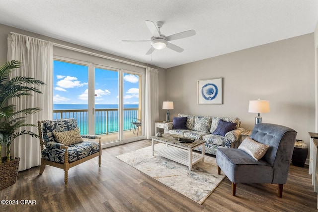 living room with a textured ceiling, a water view, hardwood / wood-style flooring, and ceiling fan