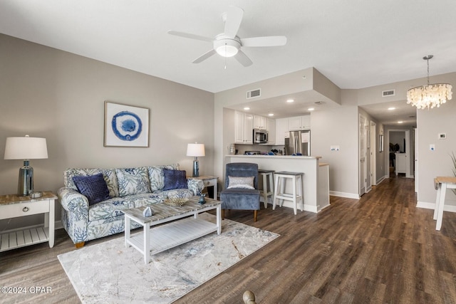 living room with ceiling fan with notable chandelier and dark hardwood / wood-style flooring