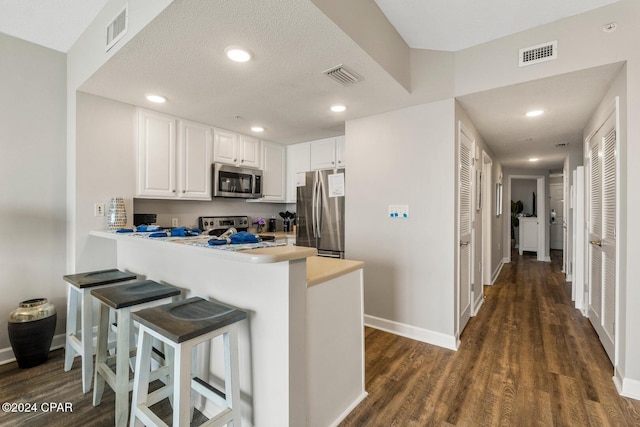 kitchen with kitchen peninsula, dark hardwood / wood-style flooring, a breakfast bar, stainless steel appliances, and white cabinets